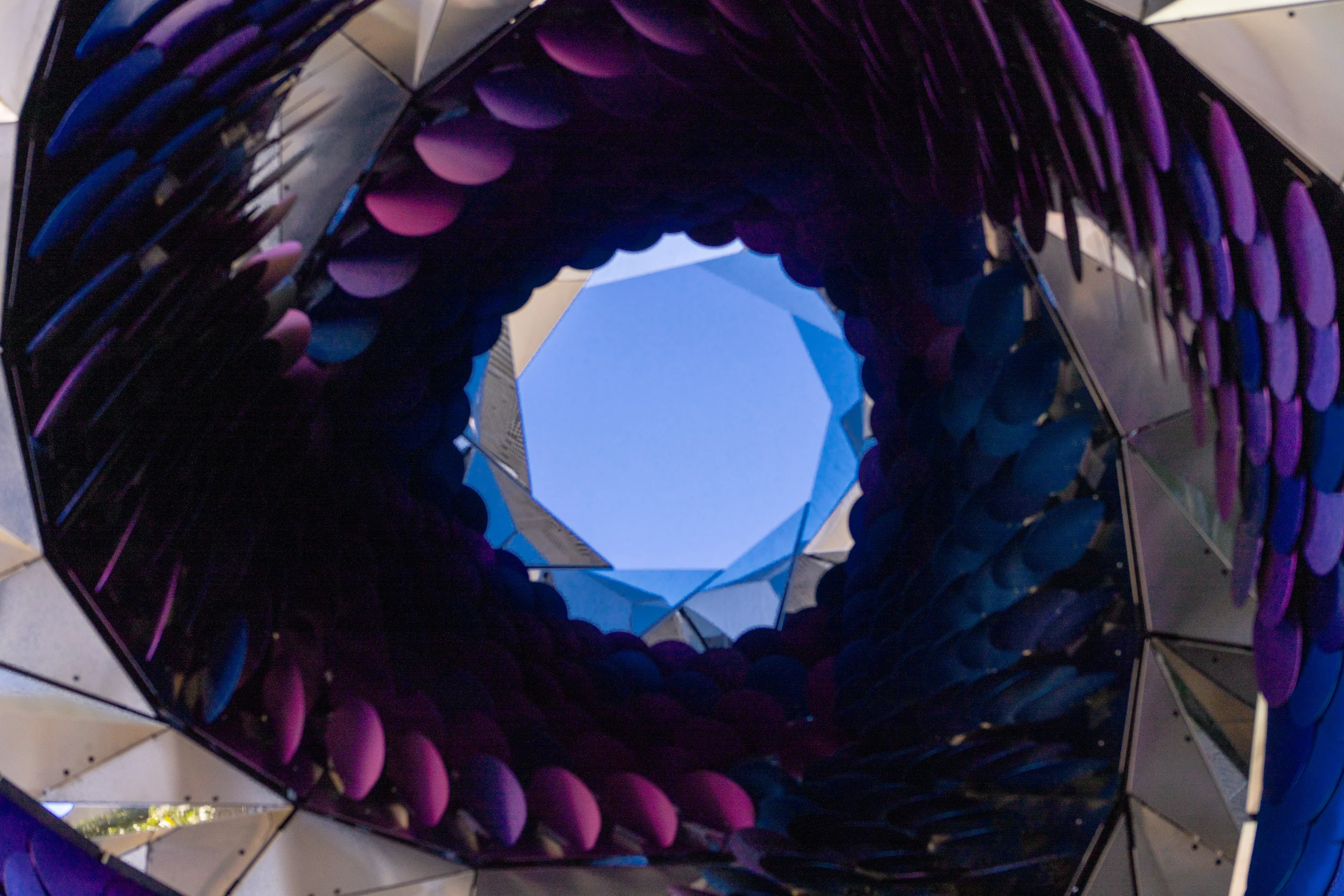 Looking up through a mirrored installation with purple spheres framing the blue sky