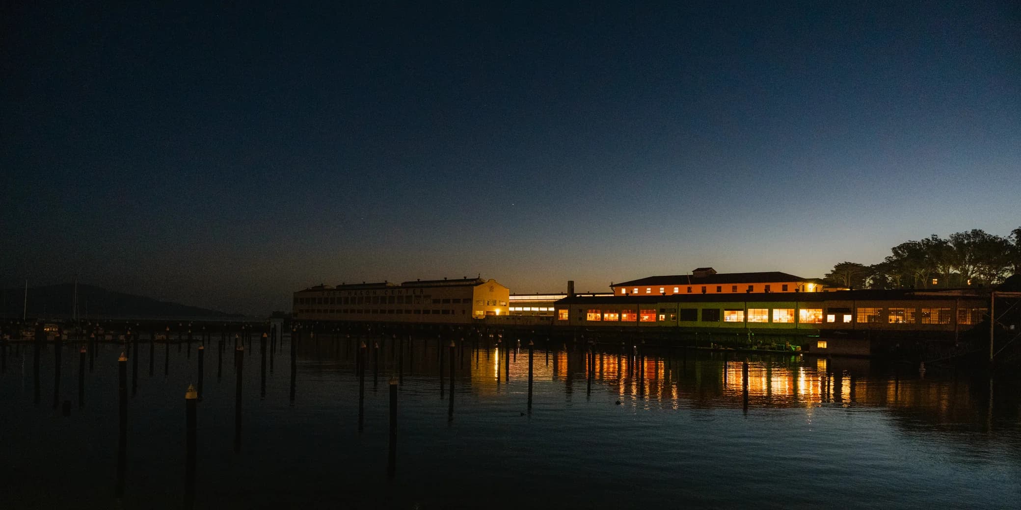 Illuminated waterfront buildings at Fort Mason reflected in the water at dusk